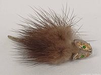 Brooch laying flat showing fur body, gold-tone head, green eyes, tail