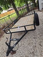 Overall side view of trailer showing wood deck, black frame, wheel, side rails