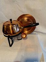 Full view of fondue pot on stand with lid, ladle hanging, and tray behind