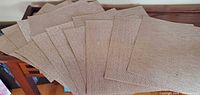 Twelve beige woven square placemats spread out to show quantity and shape
