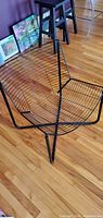 Front angled view of black wire lounge chair showing cross-base and grid seat