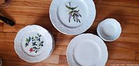 Stacks of luncheon plates, side plates and dessert bowls showing embossed rim and botanical designs