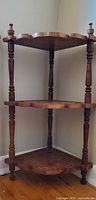 Full view of three-tier walnut corner shelf standing in corner