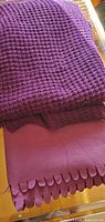 Stacked view of both purple throws showing knit texture and fleece scalloped edge