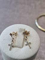 Pair of 14K gold cross earrings on display stand