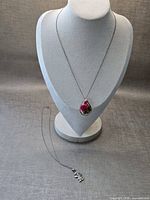 Full view of both necklaces, teardrop pendant on display bust, girl charm necklace laid flat