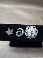 Front view of three sterling brooches: maple leaf, abstract swirl, round decorative