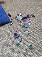 Group of mixed colored faceted stones and corner of blue Rodolfi pouch on textured surface