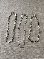 Three sterling silver bracelets laid flat showing link styles and clasps