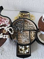 Overall view of open wooden jewelry box showing multiple compartments filled with assorted necklaces, bracelets and beads