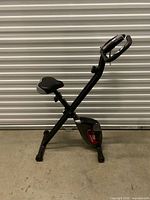 Side profile of entire Advenor folding exercise bike showing frame, seat, flywheel housing and pedals