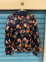 Front view of navy floral bomber jacket on hanger