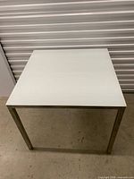 Full view of square white glass table with metal legs