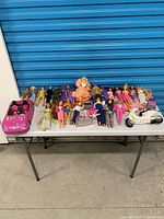 Overall lot on table showing dolls, car, scooter, accessories