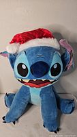 Front view of large Stitch plush wearing Santa hat