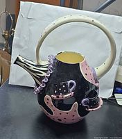 Front view of whimsical ceramic teapot with polka-dot and abstract motifs, sculpted appliqués, large loop handle
