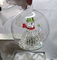 Ornament close-up showing glass tree figure, red and green accents, snowflake etching, ribbon