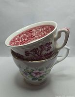 Two stacked teacups showing exterior floral design and interior red transferware