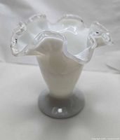 Full view of vase showing milk glass body, pedestal base, ruffled clear rim