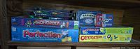 Shelf view showing Perfection, sealed Disney Monopoly, Operation, domino tin, Uno card box and additional plastic container