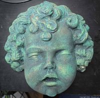 Front view of plaster cherub face sculpture showing verdigris patina and facial details