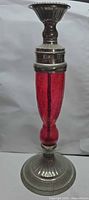 Full view of candlestick showing red glass stem and metal base