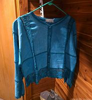 Front view of teal cardigan on hanger showing button closure and crochet trim