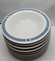 Stack of six white bowls with blue geometric rim