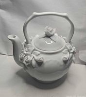 Front view of white porcelain teapot with floral accents and lid in place
