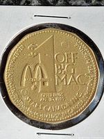 Obverse of gold-tone plastic token inside cardboard coin holder; shows design details and wear.
