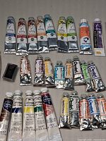 Close view of assorted watercolor paint tubes showing brands Yarka, Van Gogh, Cotman, Pentel, Grumbacher