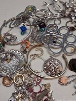Close-up of assorted silver-tone pieces, rhinestone brooches, hoop earrings and charms