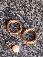 two gold-tone hoop earrings and pearl charm on granite surface