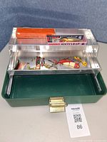 Open green Umco 102U tackle box with aluminum trays showing assorted loose lures and two boxed Rapala crankbaits