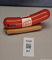 Full side view of red and tan plastic Wienermobile coin bank with Oscar Mayer decal