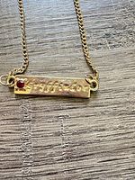 Close-up of bar pendant showing Gryffindor engraving and red stone