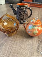 All three items grouped together on floor—porcelain sugar bowl, amber glass basket, carved wooden pitcher