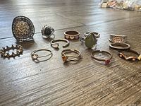 All 12 rings arranged on wooden surface, showing variety of styles and finishes
