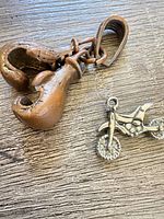 Bronze-tone boxing glove and boot charms next to silver-tone motorcycle charm