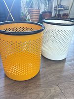 Yellow and white perforated metal wastebaskets side by side