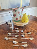 Group shot of all items: moka pot, floral teapot, yellow hive creamer, twelve teaspoons