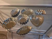 Assorted aluminum tartlet molds on glass table, multiple shapes visible
