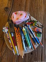 Group of assorted pens, pencils, erasers, sharpener and pouch on wooden surface