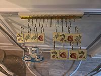 Shower hooks with ceramic tiles on wood/brass rail and teapot wall hook beneath