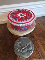 Pincushion displayed on stand with metal tin beside