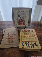 Overall lot showing three visible items: two hardcover children’s books and a vintage composition book with a grey notebook behind