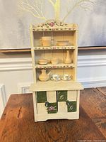Full view of beige and green miniature hutch with wooden and porcelain accessories