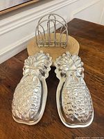 Pair of aluminum pineapple molds and metal napkin rack on table