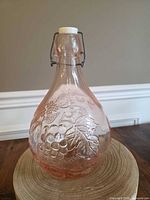 Front view of pink glass bottle showing grape embossing and swing-top