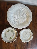 Large white cabbage leaf platter, small cabbage leaf side plate, and one floral salad plate displayed on wooden table